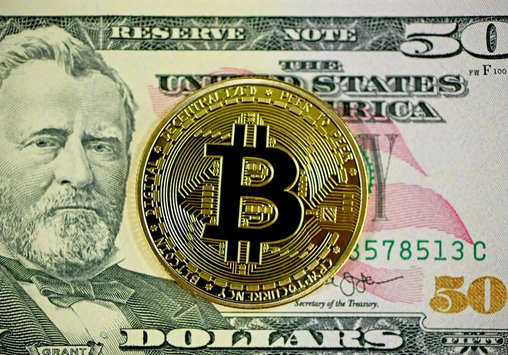 Bitcoin coin on US fifty-dollar bill.